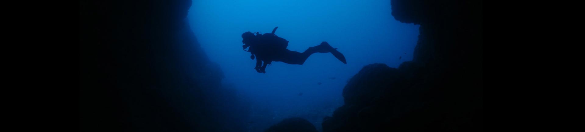 Night diver swimming on the outside of the cave entrance